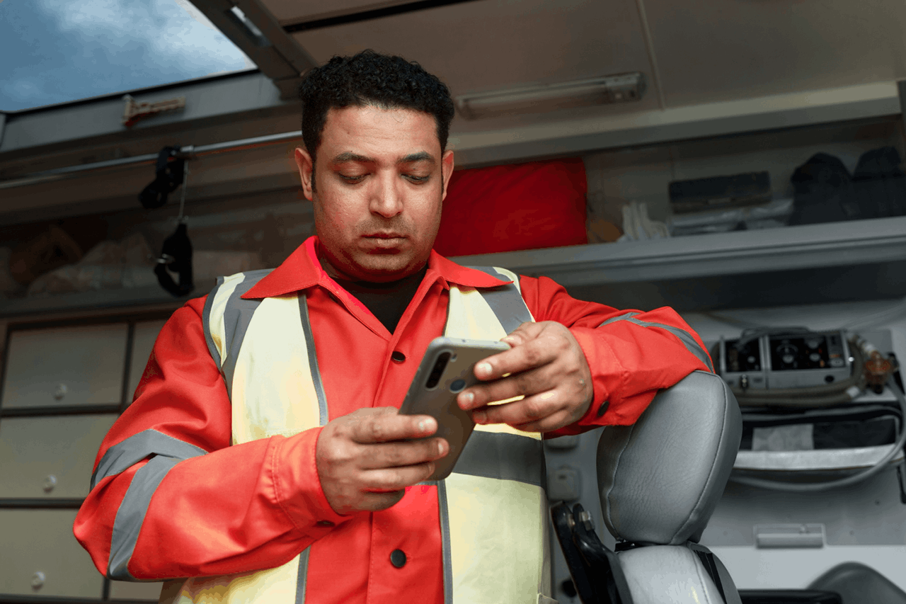 An emergency worker using his smartphone in front of an emergency vehicle.
