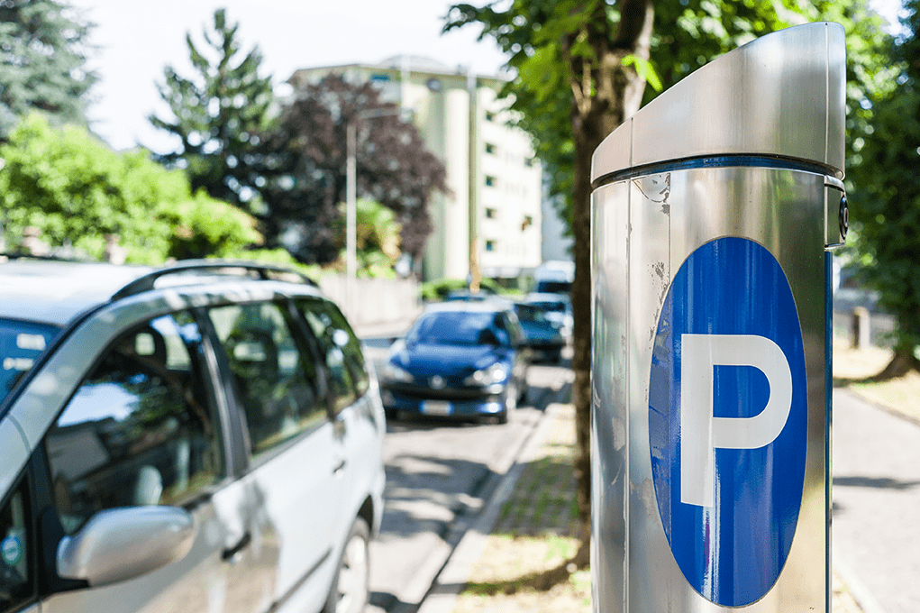 A parking meter on a street with parked cars.