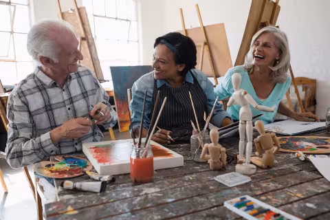 Senior citizens laughing and painting at an art workshop.