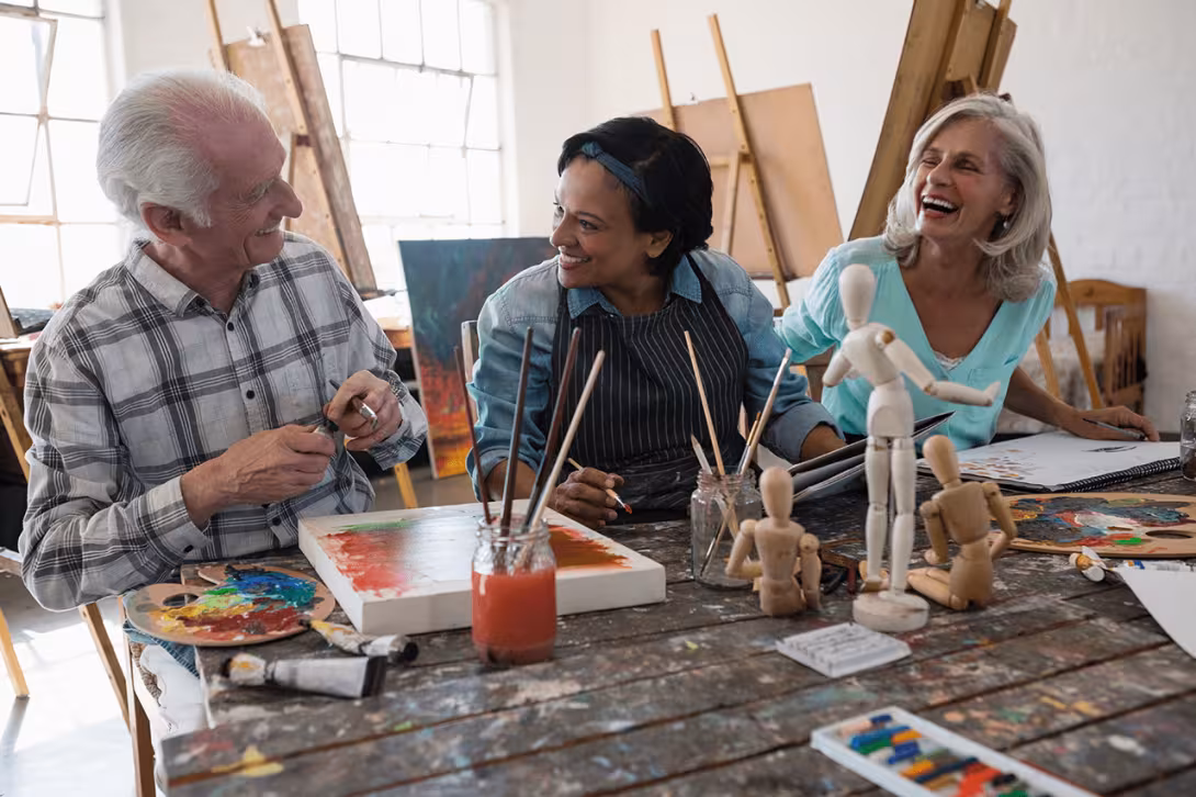 Senior citizens laughing and painting at an art workshop.