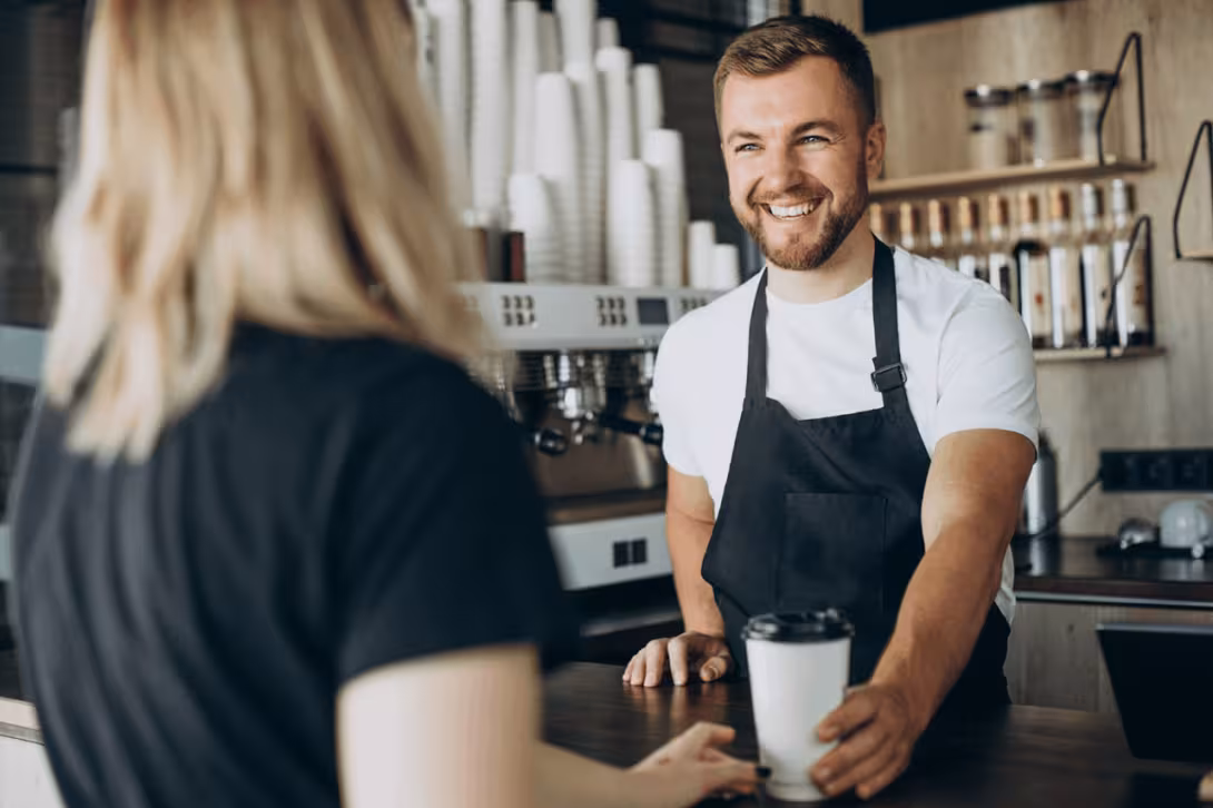 A barista serving coffee to a customer in a caf&eacute;.